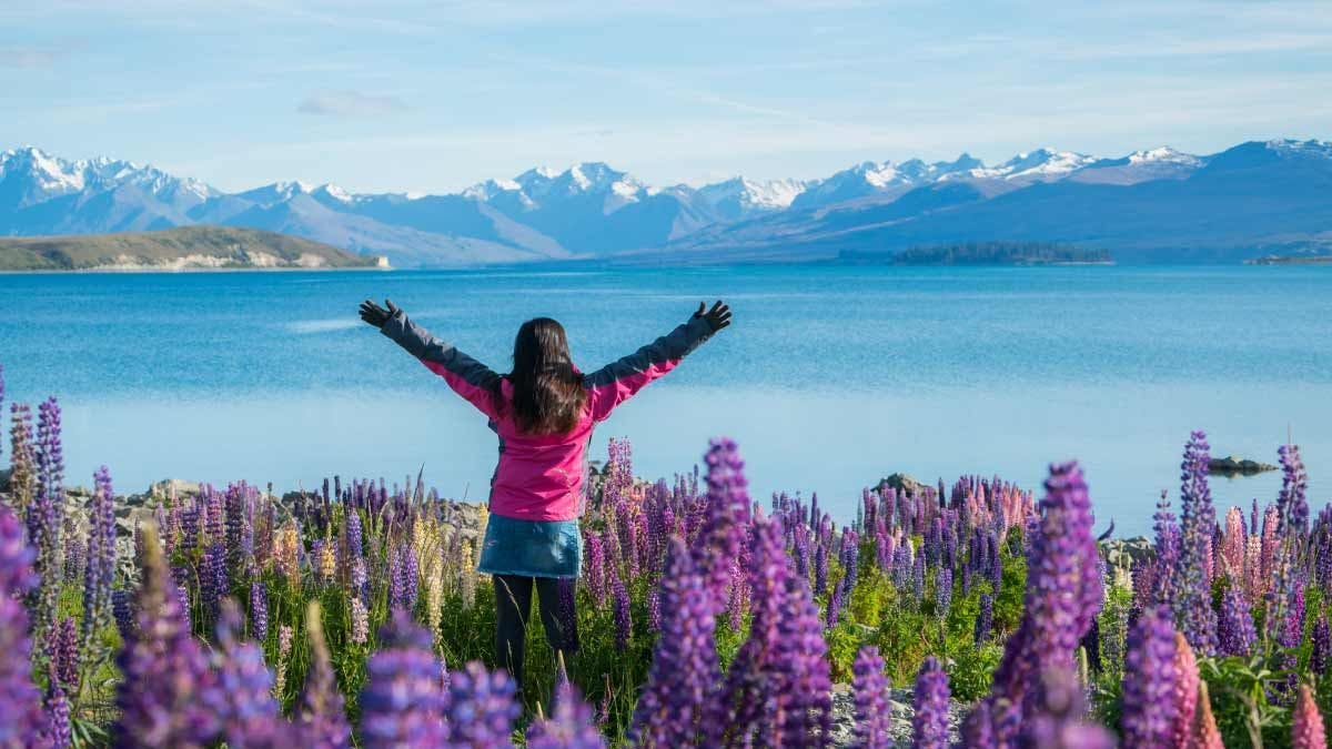 Woman standing amongst lupin flowers in front of Lake Tekapo
