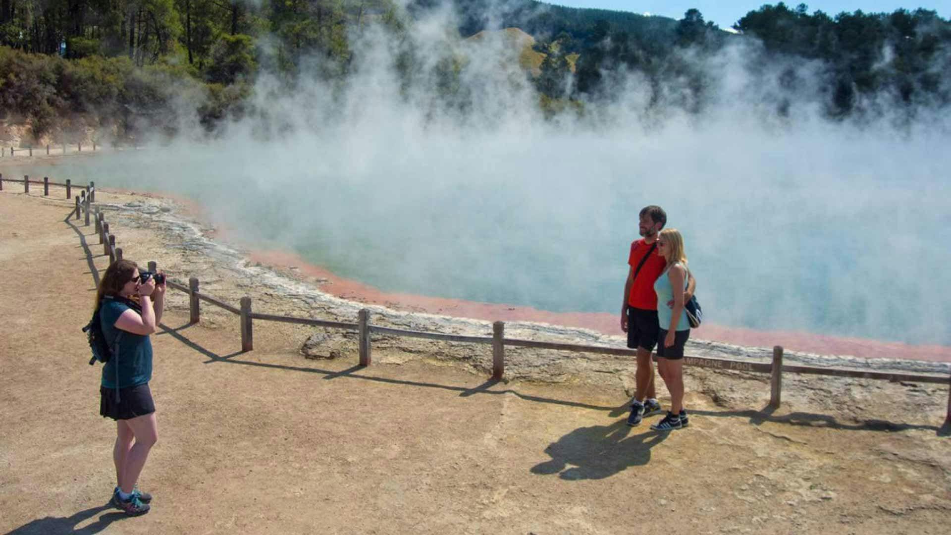 Couple pose for a picture in front of a geothermal lake in Rotorua