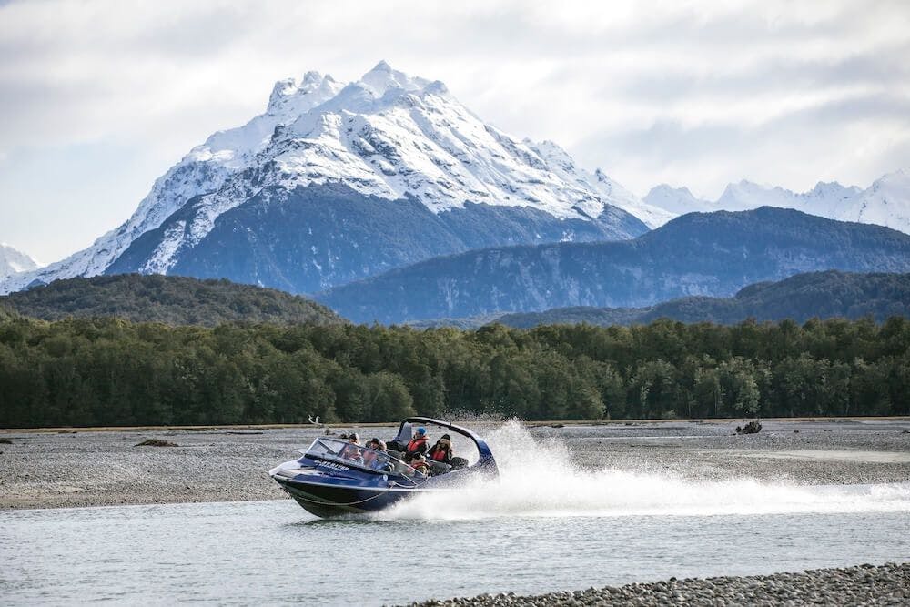 A jetboat on a river in Queenstown New Zealand in winter with snowy mountains.