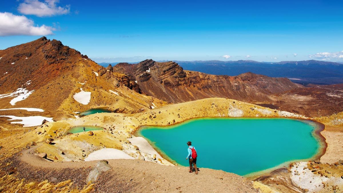Person walks in front of the Emerald Lakes on the Tongariro Crossing
