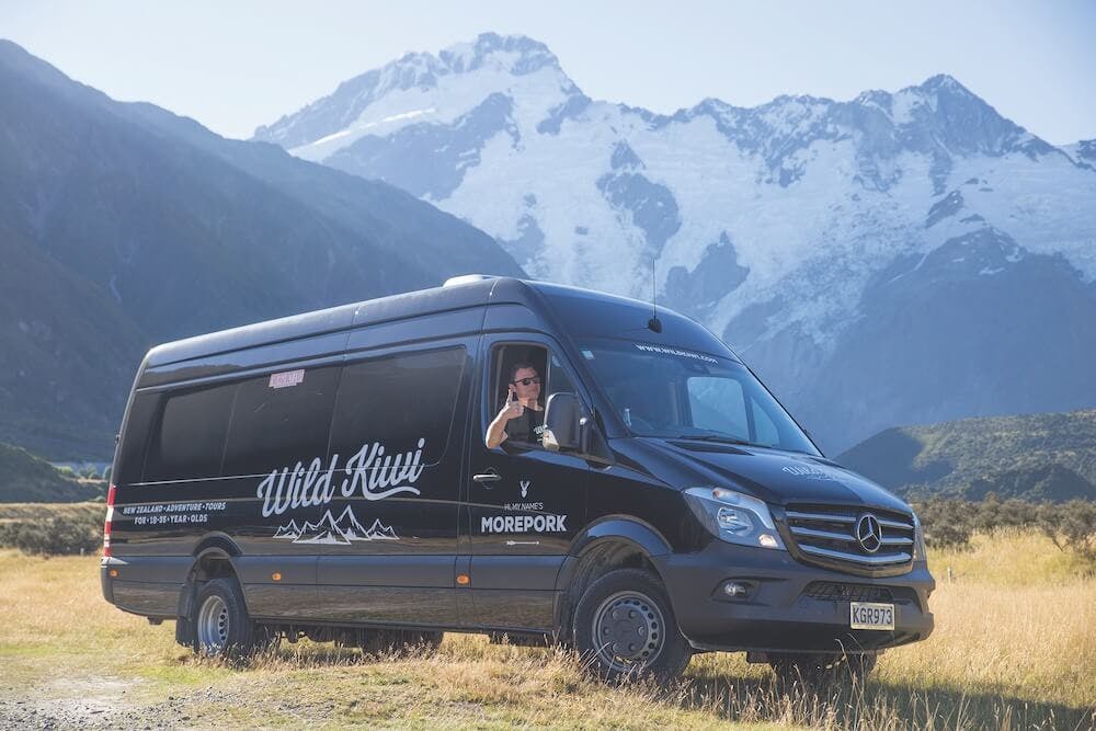 A New Zealand luxury tour van of Wild Kiwi in a field with mountains behind during winter in New Zealand.