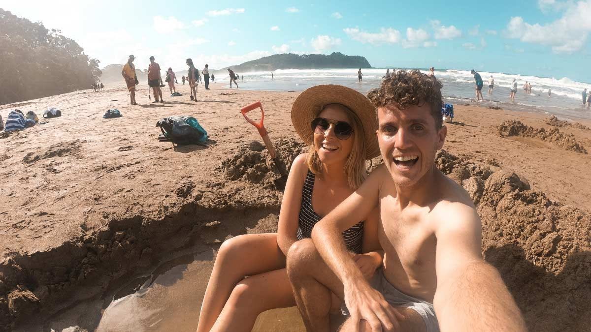 Couple sitting in a hole in the sand at Hot Water Beach