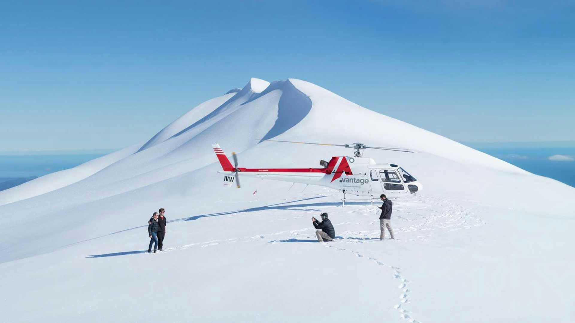 People getting a photo on the top of a mountain next to their helicopter