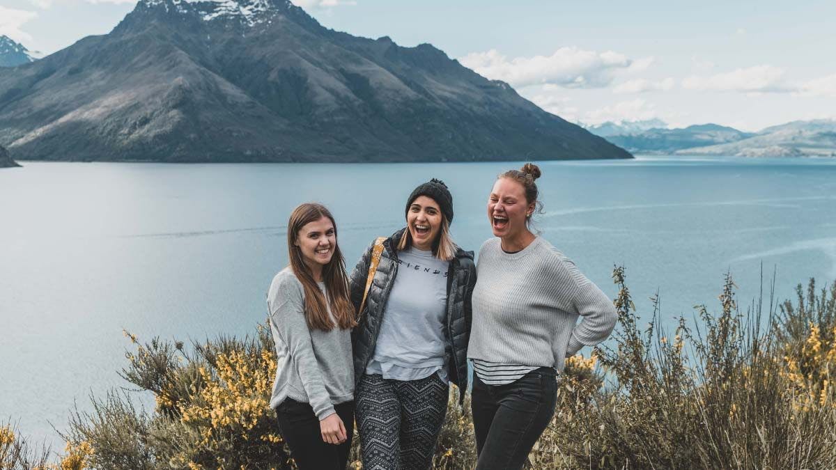 Three friends standing in front of Lake Wakatipu in New Zealand