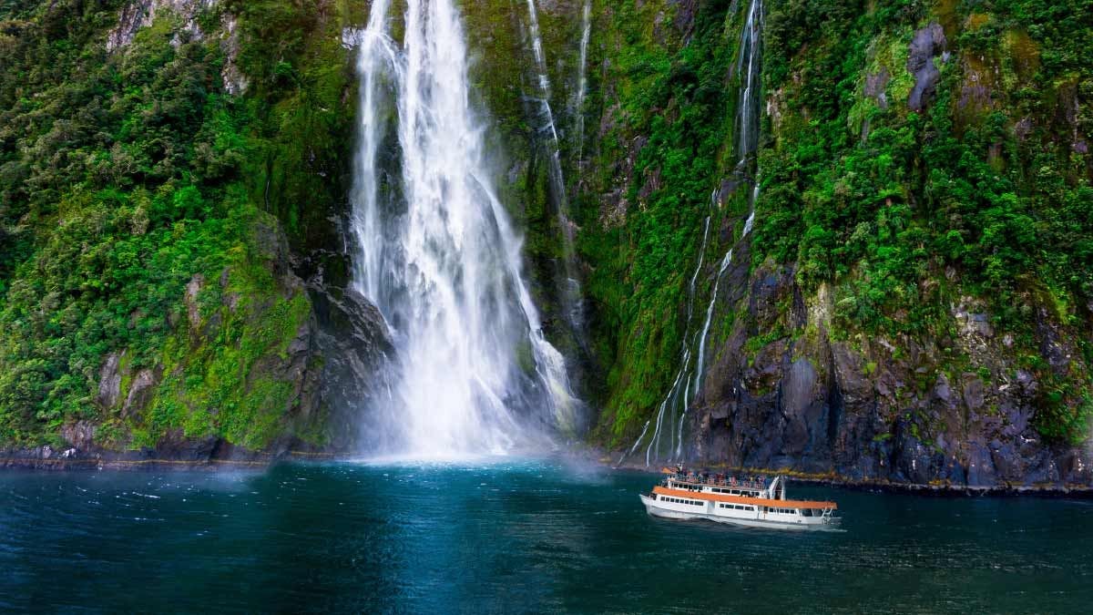 Boat next to a huge waterfall in Milford Sound