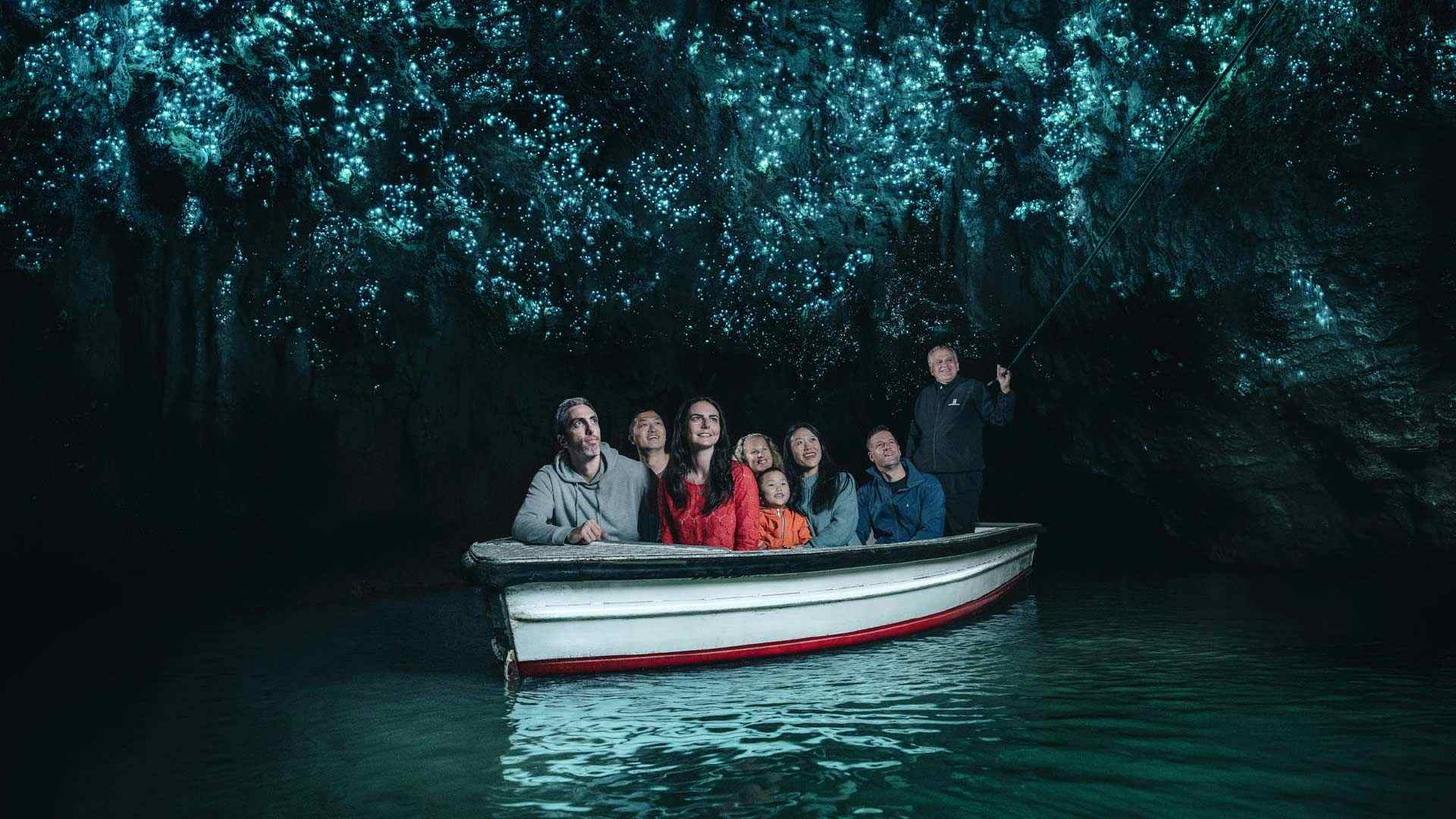 Group of people take a boat tour through glow worm caves