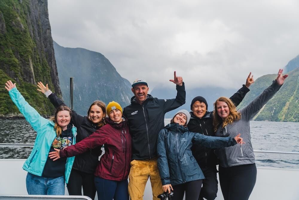 A group of travellers with hands in the air happy while on a Milford Sound cruise in New Zealand in winter.