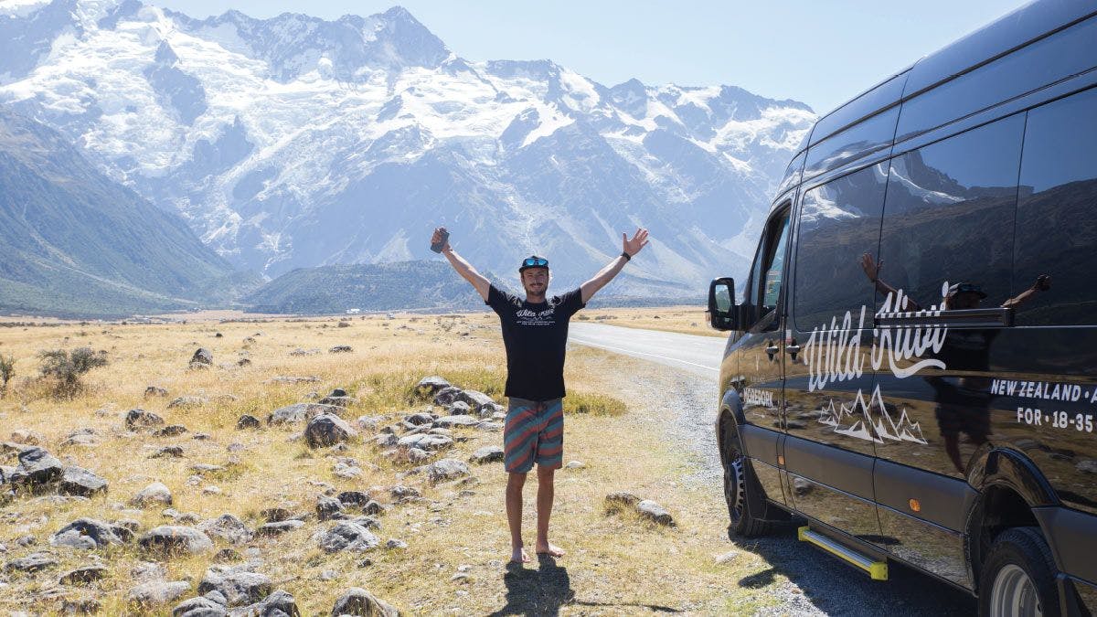 Wild Kiwi guide stood next a tour vehicle in front of some mountains in New Zealand