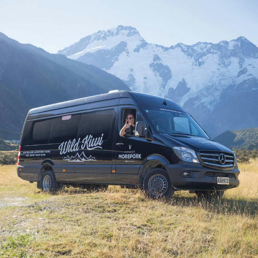 Wild Kiwi bus parked in front of some beautiful mountains